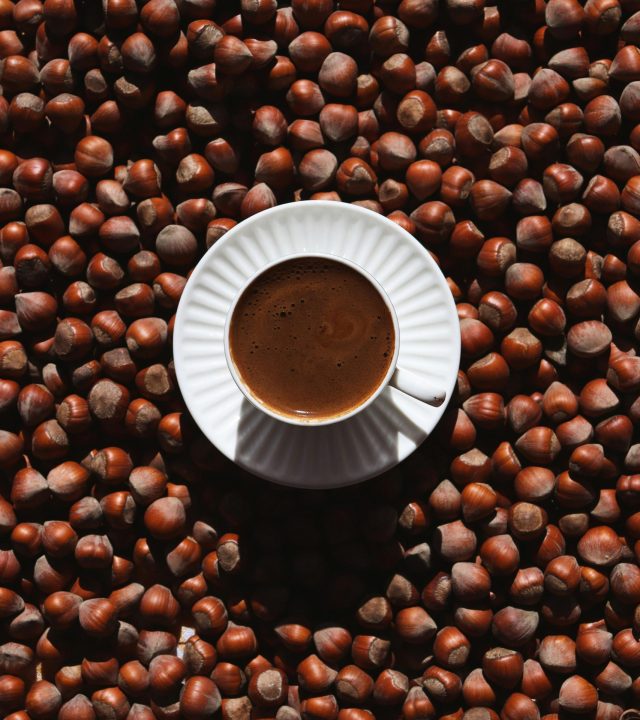 Top view of a coffee cup placed among scattered hazelnuts, highlighting rich textures.