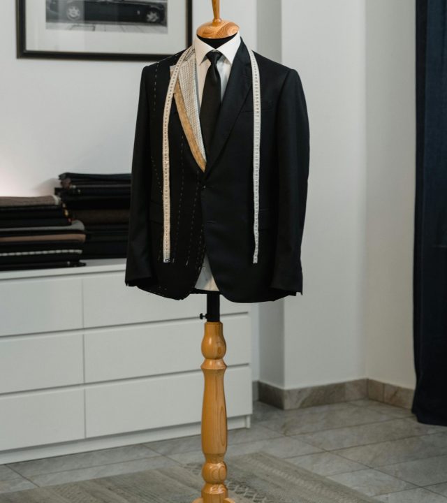 A stylish black suit jacket displayed on a mannequin with a measuring tape, showcasing bespoke tailoring in an elegant studio setting.
